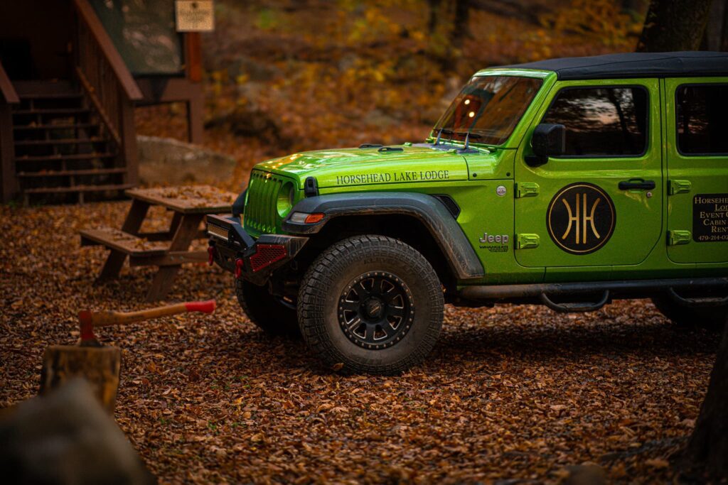 A green jeep is parked in the woods.