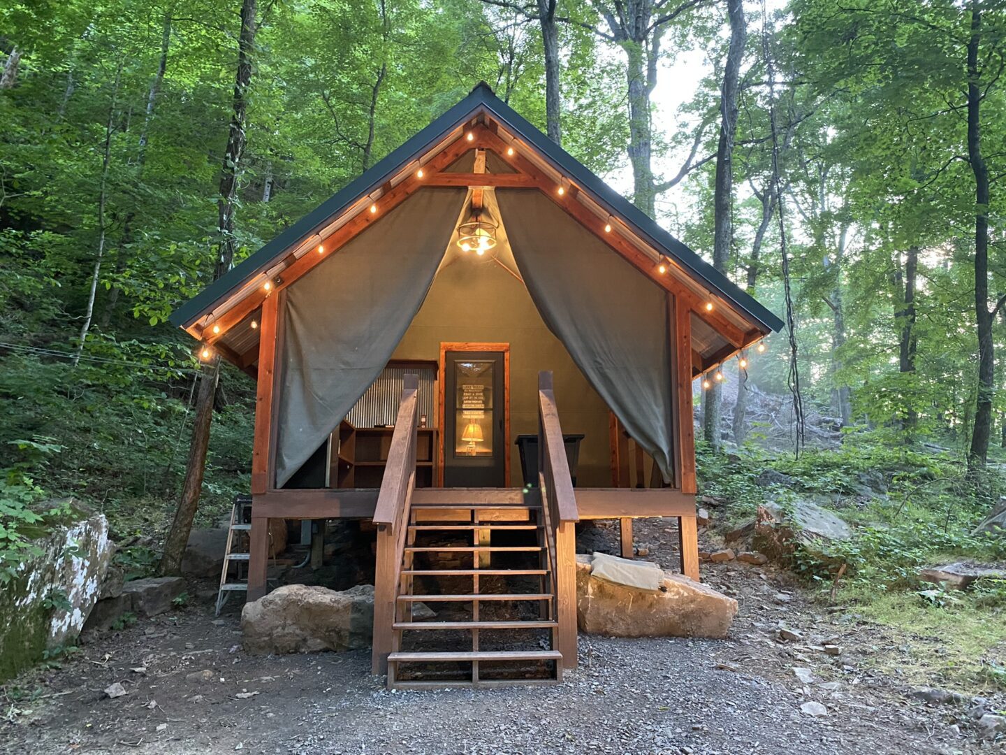 A tent in the woods with lights on.