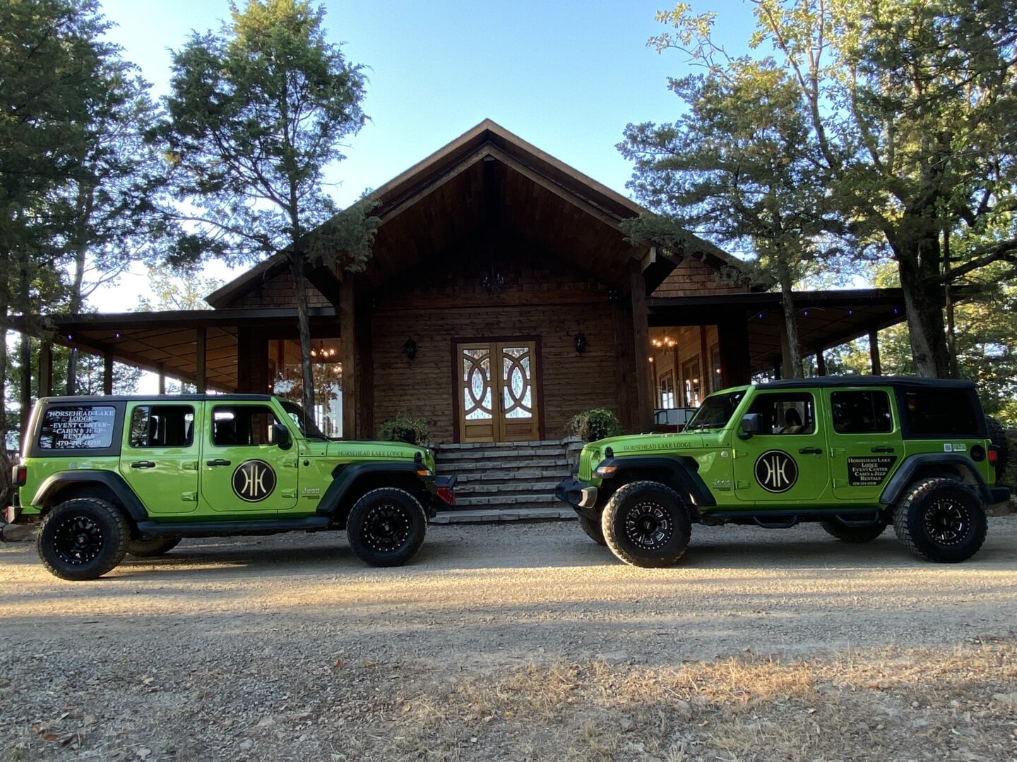 Two green jeep wranglers parked in front of a building.