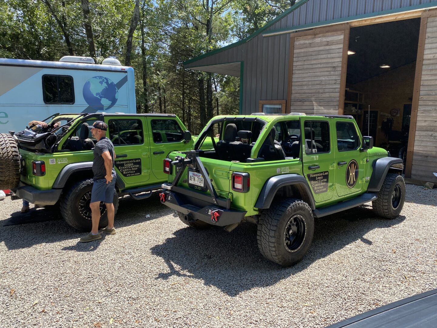 Two green jeep wranglers parked in a gravel lot.