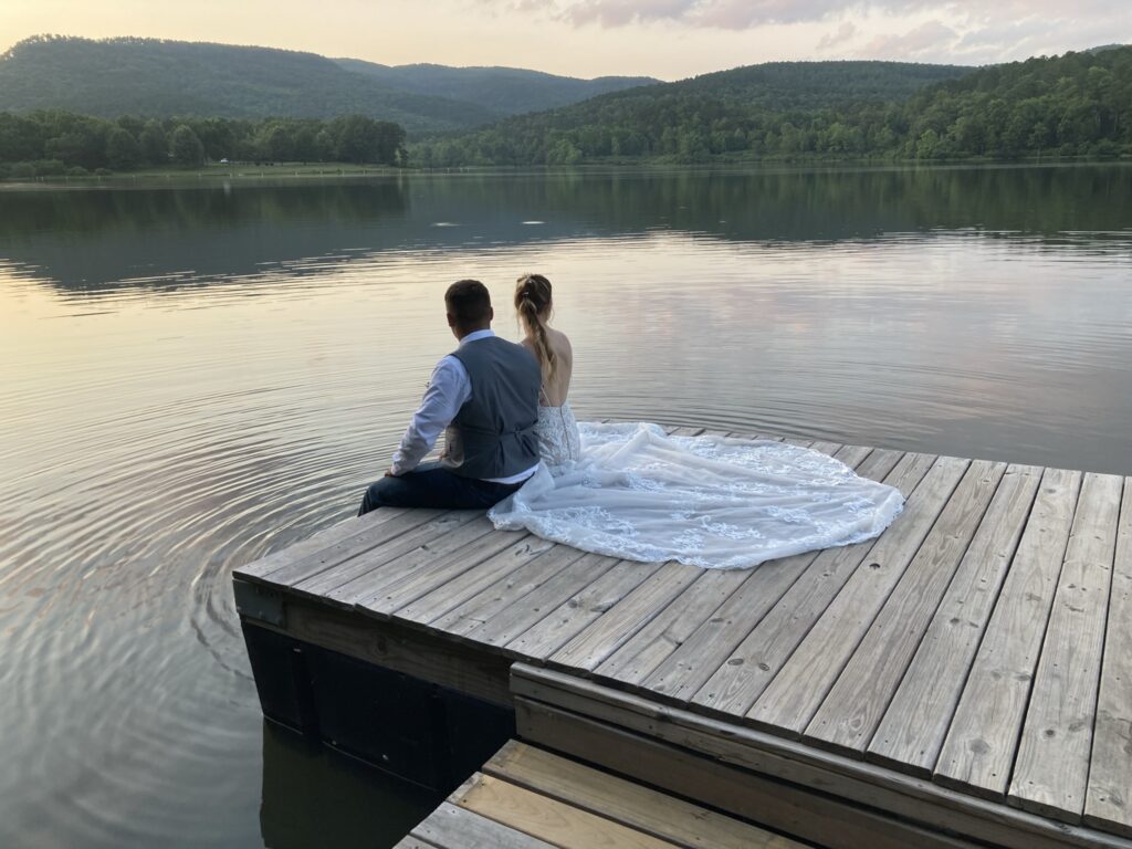 A man and woman sitting on the dock of a lake.